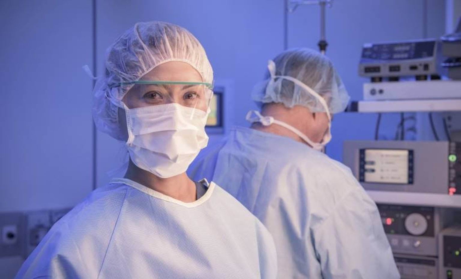female doctor wearing gown, cap, mask, and protective eyewear and looking at camera prior to start of surgery