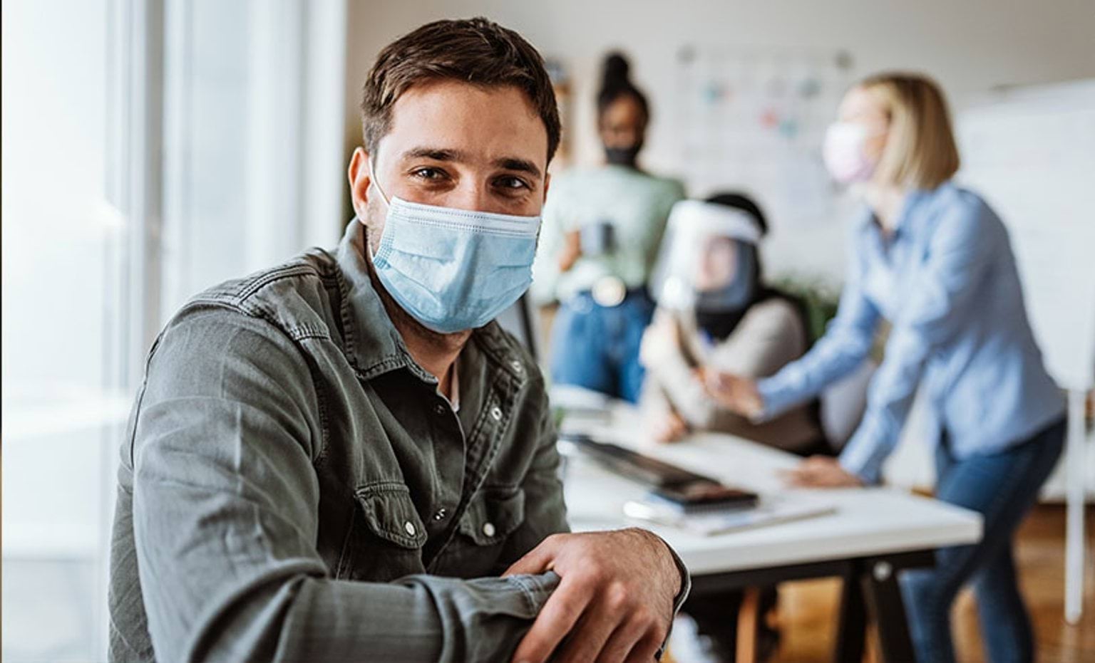 man in mask with team behind him at desk