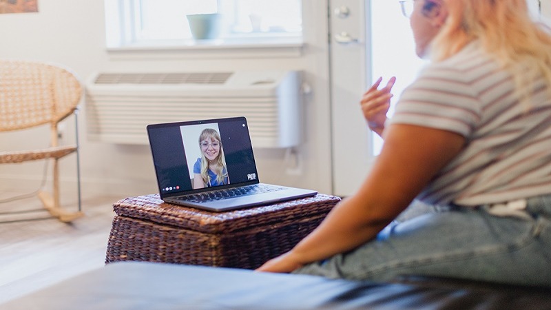 A women talking to her computer, as she is having a virtual appointment with a female nurse.