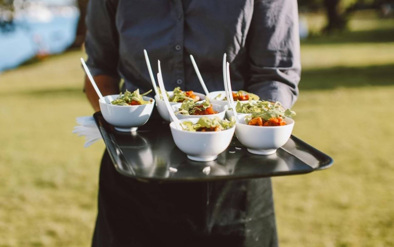 A server holding a tray of white bowls with food in them.