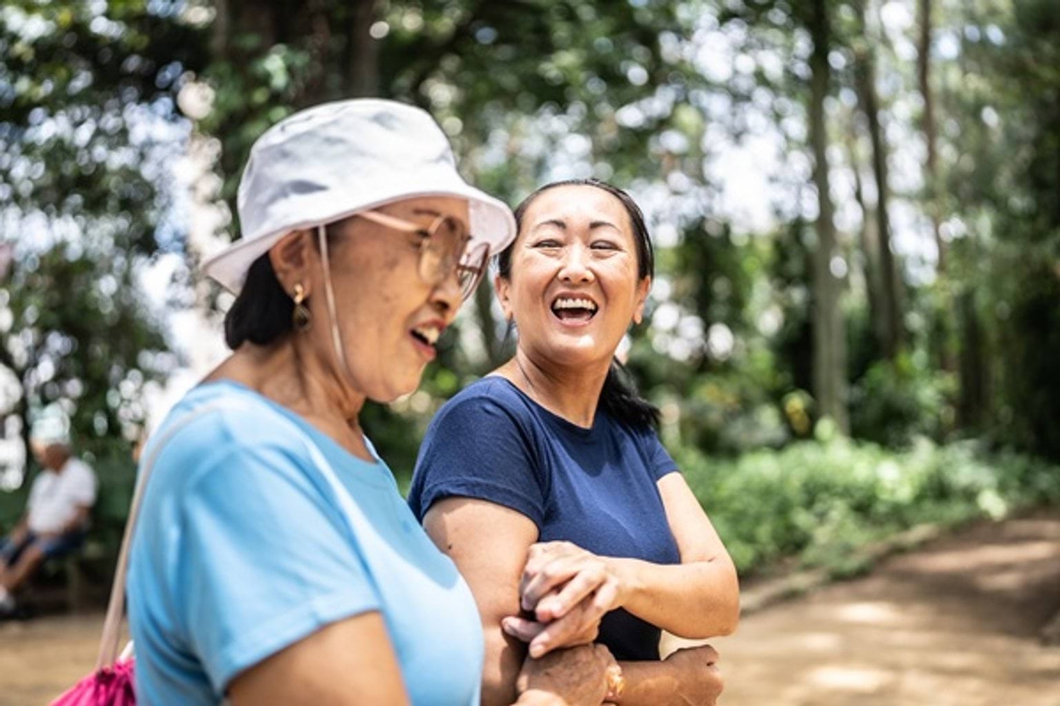 Two women walking in the bush, smiling at each other as they hold hands.