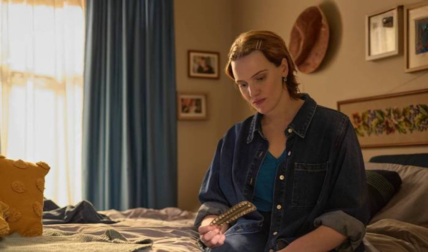 A person sitting on a bed looking at an empty pill packet