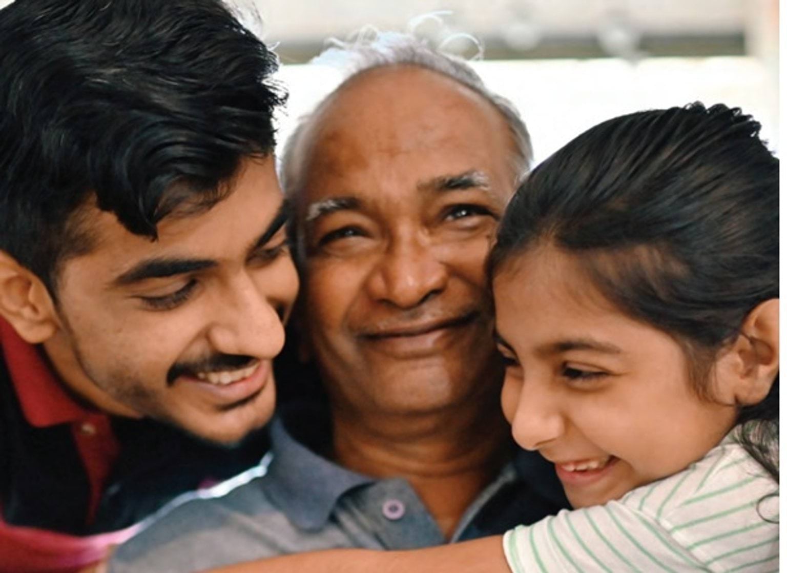 Two young people hugging an elderly man.