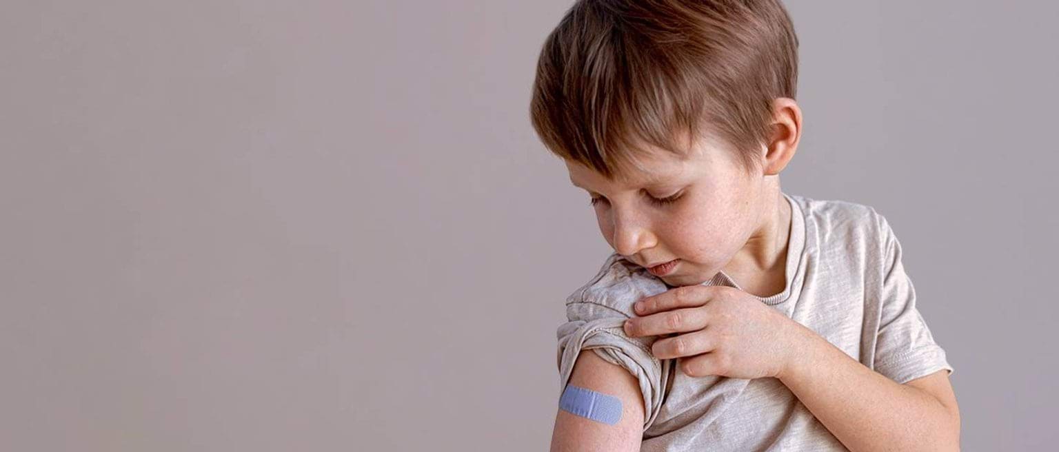 A boy looks down at a bandaid on his arm after vaccination