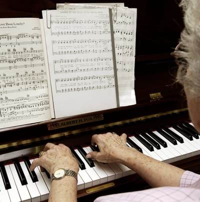 An older woman is playing piano. People with dementia should be encourage to do meaningful activities. 
